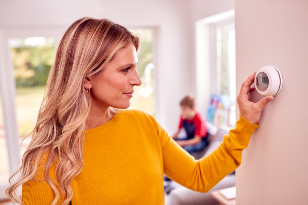 Mother At Home With Son Adjusting Smart  Thermostat Control