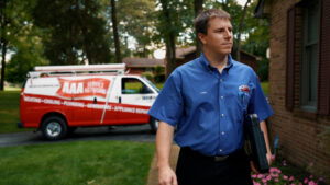 A technician from AAA Service Networks approaches a home for a sewer camera inspection. Behind him in the driveway is a branded service van.