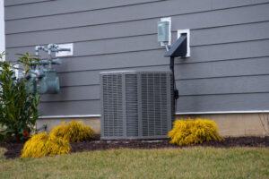 An AC units sits by a home surrounded by attractive landscaping.