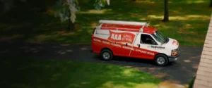 A red and white AAA Service Network van is parked on a driveway surrounded by green grass and trees.