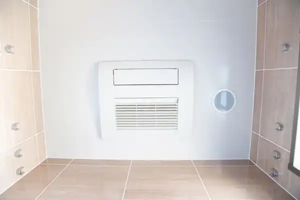 A white wall-mounted ventilation unit with an air vent, expertly installed by AAA Service Network, in a tiled room with light brown floors and walls.