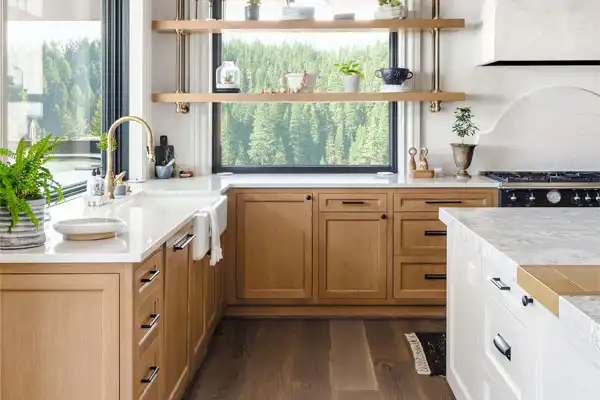 A bright, modern kitchen serviced by AAA Service Network: light wood cabinets, white counters, gold faucet, plants, and forest view.