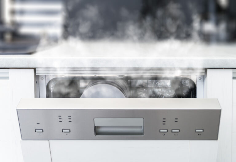 An open dishwasher releases steam, with clean dishes visible inside and condensation on the door—a scene familiar before needing Dishwasher Repair.
