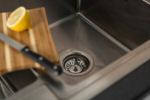 A stainless steel kitchen sink with a knife and a wooden cutting board holding a halved lemon rests on the edge, showcasing smart organization and offering subtle plumbing tips for maintaining a tidy, efficient workspace.